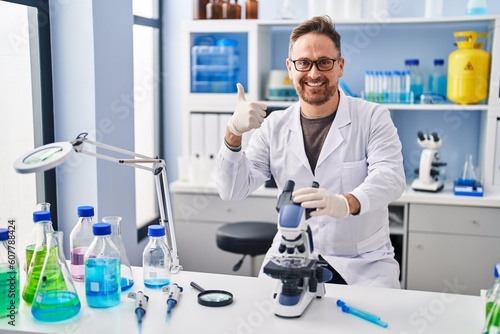 Middle age caucasian man working at scientist laboratory smiling happy and positive  thumb up doing excellent and approval sign