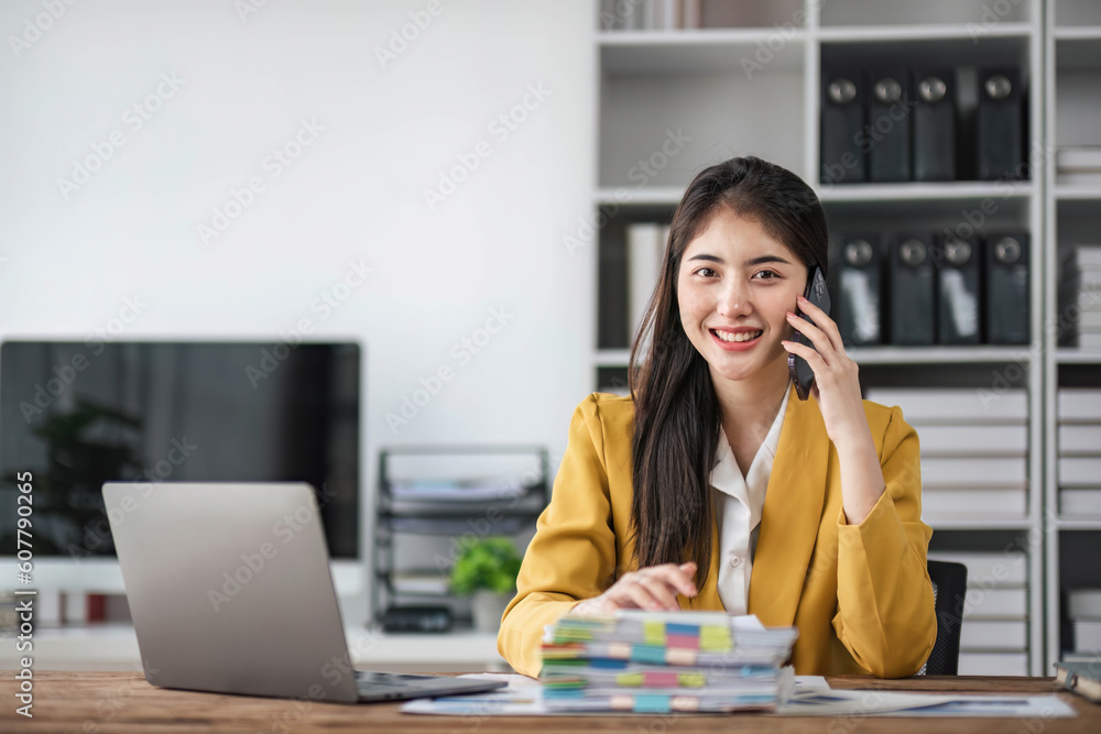 Young busy asian business woman talking on phone working in modern office. Asian businesswoman company sales client manager wearing suit making call on cellphone sitting at workplace. Young busy asian business woman talking on phone working in modern office. Asian businesswoman company sales client manager wearing suit making call on cellphone sitting at workplace.