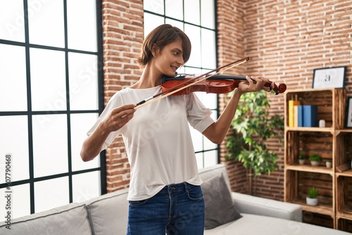 Young beautiful hispanic woman musician smiling confident playing violin at home