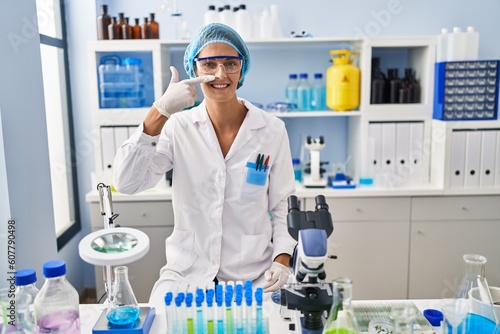Brunette woman working at scientist laboratory pointing with hand finger to face and nose  smiling cheerful. beauty concept