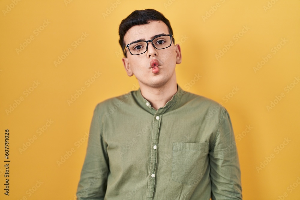 Obraz premium Non binary person standing over yellow background making fish face with lips, crazy and comical gesture. funny expression.
