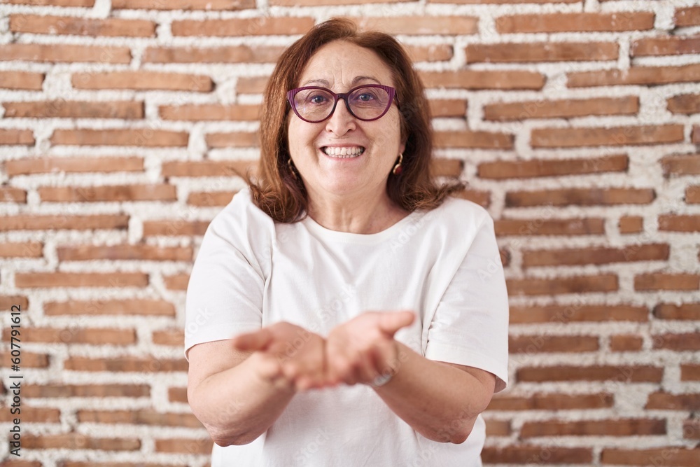 Senior woman with glasses standing over bricks wall smiling with hands palms together receiving or giving gesture. hold and protection Senior woman with glasses standing over bricks wall smiling with hands palms together receiving or giving gesture. hold and protection