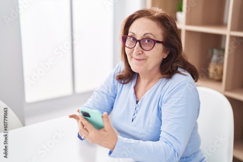 Senior woman using smartphone sitting on table at home