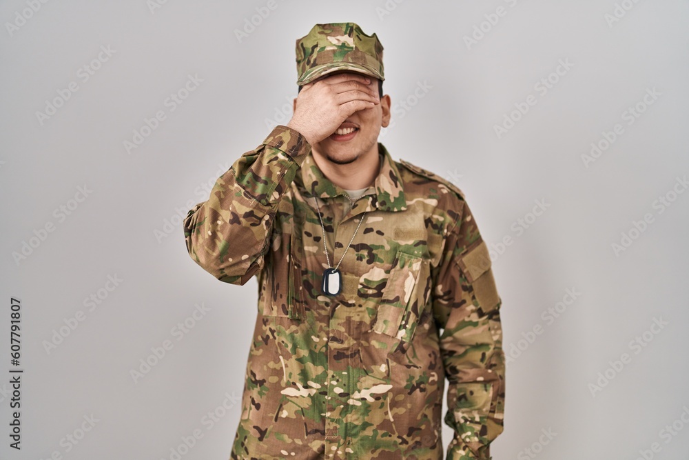 Young arab man wearing camouflage army uniform smiling and laughing with hand on face covering eyes for surprise. blind concept. Young arab man wearing camouflage army uniform smiling and laughing with hand on face covering eyes for surprise. blind concept.