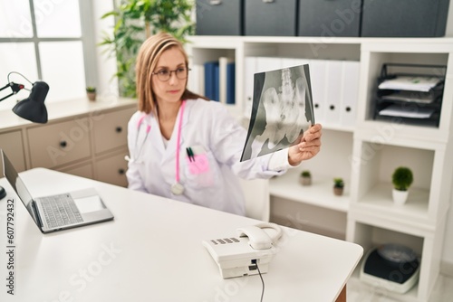 Young blonde woman doctor using laptop holding xray at clinic