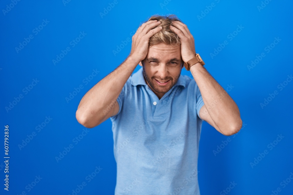 Caucasian man standing over blue background suffering from headache desperate and stressed because pain and migraine. hands on head. Caucasian man standing over blue background suffering from headache desperate and stressed because pain and migraine. hands on head.