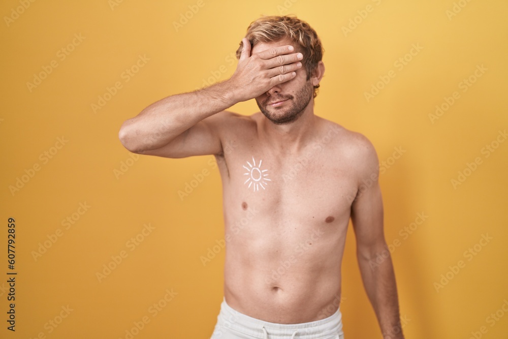 Caucasian man standing shirtless wearing sun screen covering eyes with hand, looking serious and sad. sightless, hiding and rejection concept