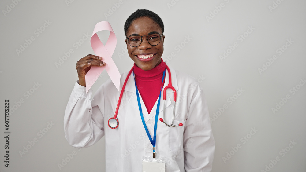 African american woman doctor holding breast cancer awareness pink ribbon over isolated white background African american woman doctor holding breast cancer awareness pink ribbon over isolated white background