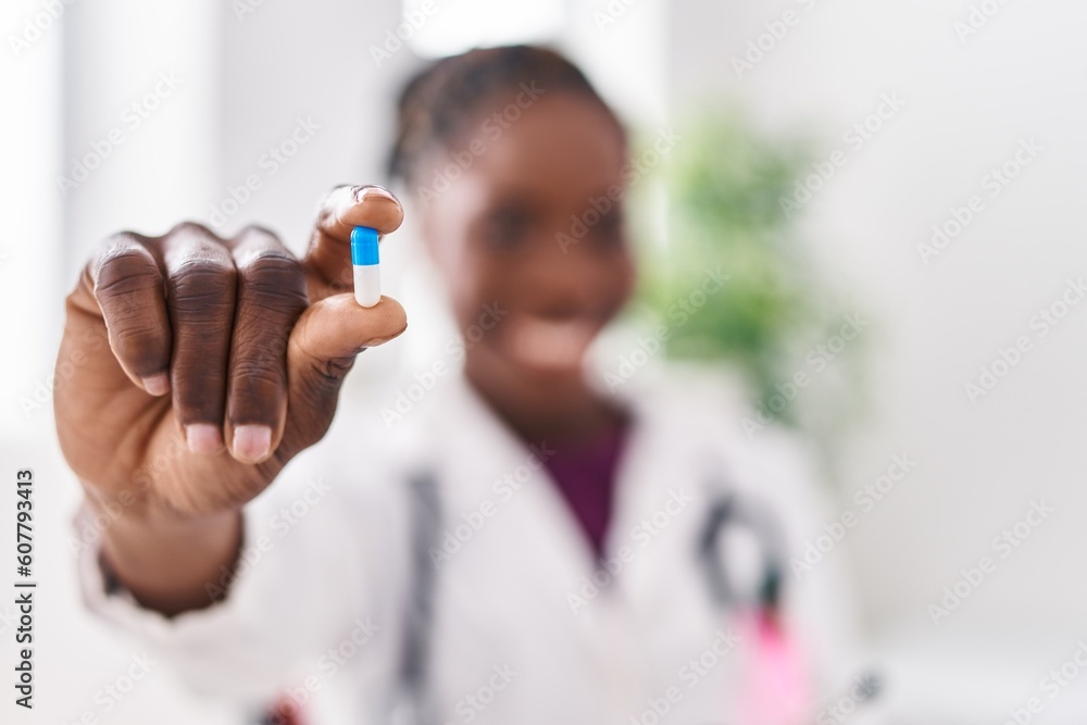 African american woman wearing doctor uniform holding pill at clinic African american woman wearing doctor uniform holding pill at clinic