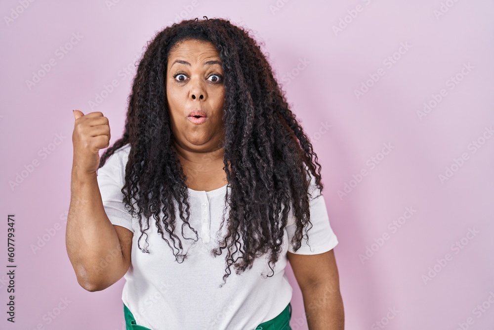 Plus size hispanic woman standing over pink background surprised pointing with hand finger to the side, open mouth amazed expression. Plus size hispanic woman standing over pink background surprised pointing with hand finger to the side, open mouth amazed expression.