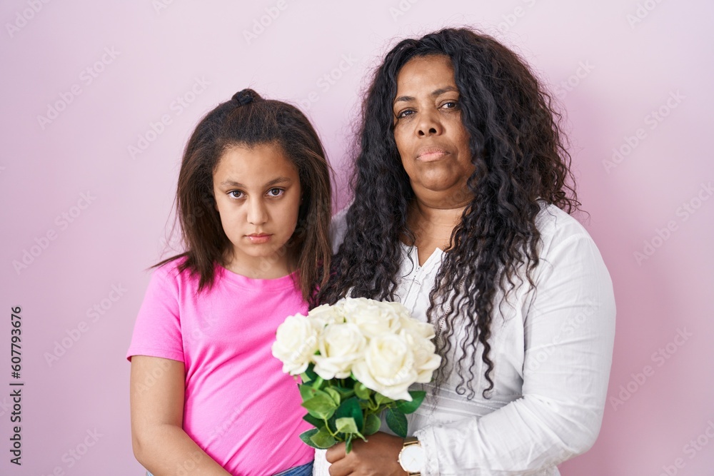 Mother and young daughter holding bouquet of white flowers relaxed with serious expression on face. simple and natural looking at the camera. Mother and young daughter holding bouquet of white flowers relaxed with serious expression on face. simple and natural looking at the camera.