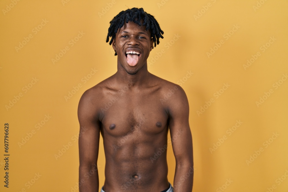 Young african man with dreadlocks standing shirtless sticking tongue out happy with funny expression. emotion concept.