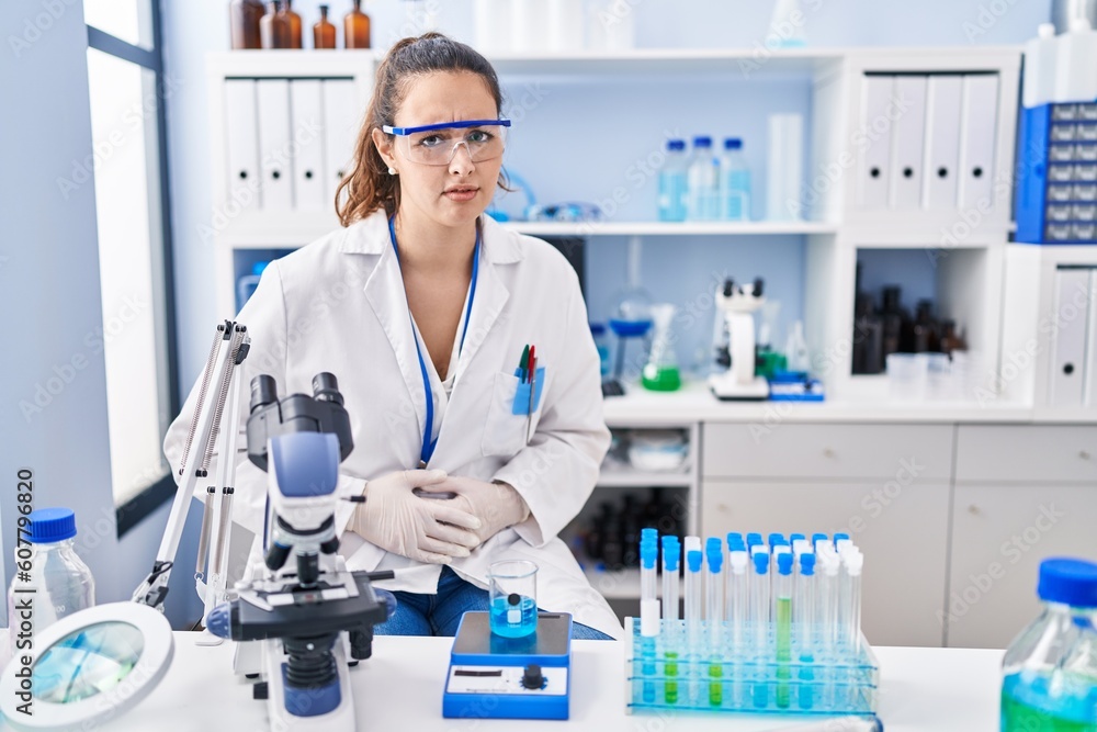 Young hispanic woman working at scientist laboratory with hand on stomach because nausea, painful disease feeling unwell. ache concept. Young hispanic woman working at scientist laboratory with hand on stomach because nausea, painful disease feeling unwell. ache concept.
