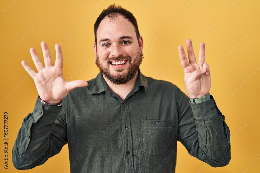 Plus size hispanic man with beard standing over yellow background showing and pointing up with fingers number eight while smiling confident and happy. Plus size hispanic man with beard standing over yellow background showing and pointing up with fingers number eight while smiling confident and happy.