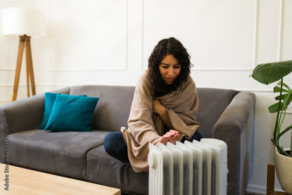 Cold young woman turning on the electric heater at home