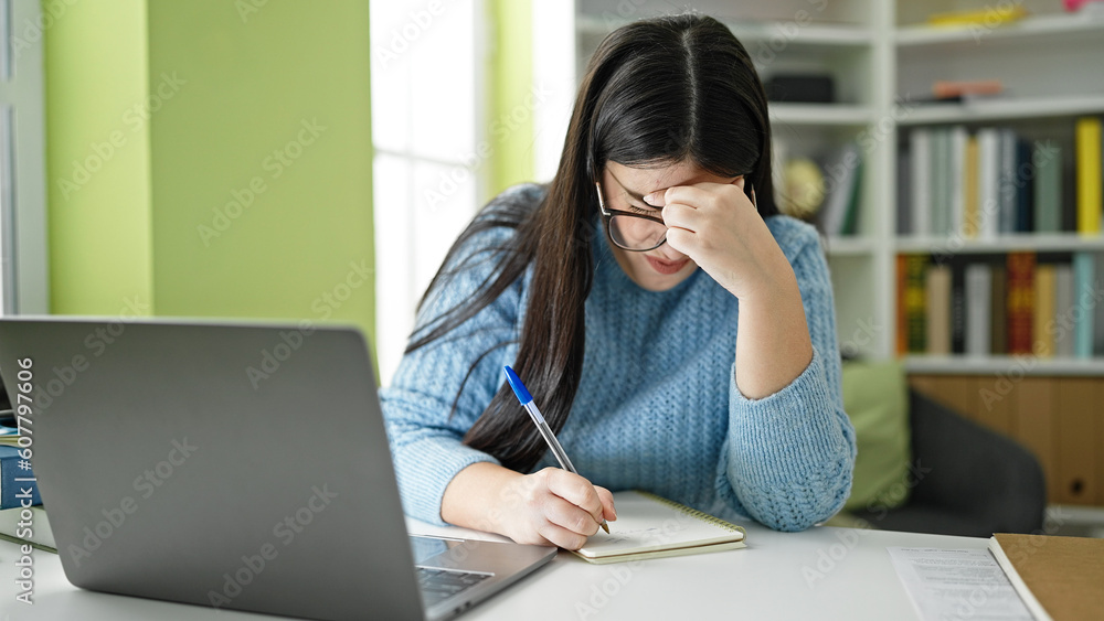 Young hispanic woman student tired using laptop and taking notes at library university Young hispanic woman student tired using laptop and taking notes at library university