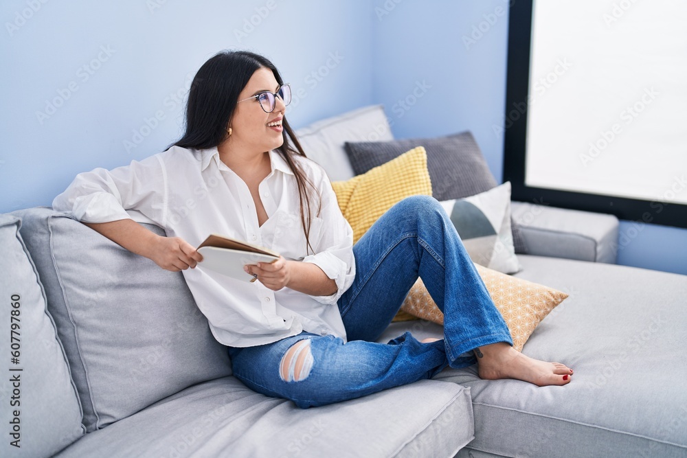 Young hispanic woman reading notebook sitting on sofa at home Young hispanic woman reading notebook sitting on sofa at home