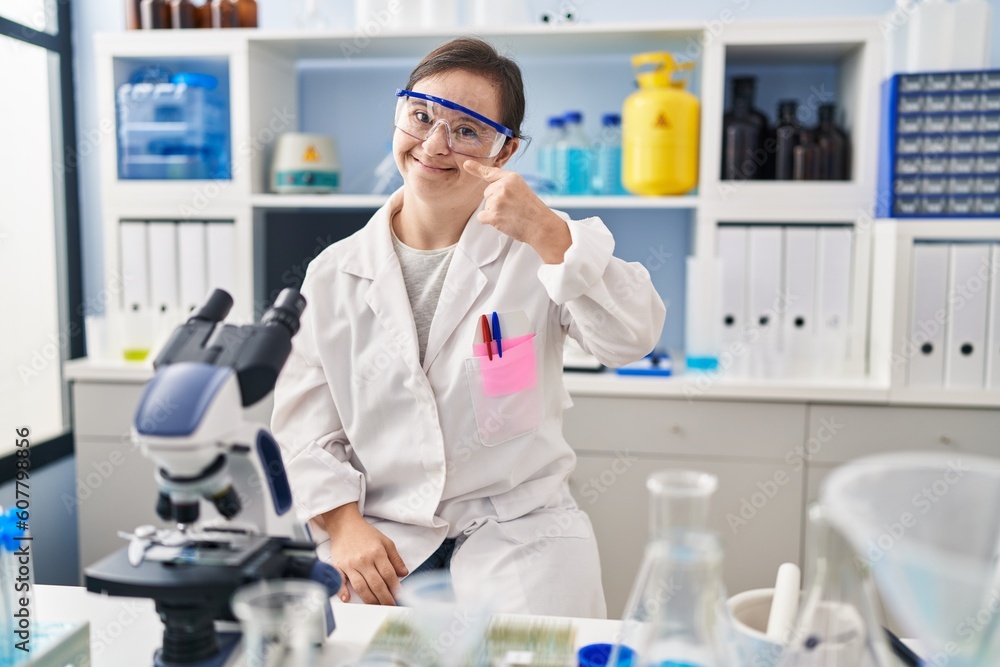 Hispanic girl with down syndrome working at scientist laboratory pointing with hand finger to face and nose, smiling cheerful. beauty concept Hispanic girl with down syndrome working at scientist laboratory pointing with hand finger to face and nose, smiling cheerful. beauty concept