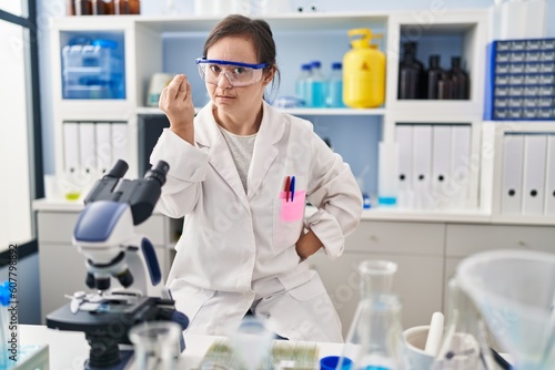 Hispanic girl with down syndrome working at scientist laboratory doing italian gesture with hand and fingers confident expression
