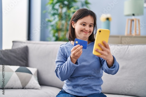 Young woman with down syndrome using smartphone and credit card sitting on sofa at home