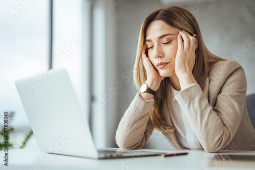 Female entrepreneur with headache sitting at desk. Businesswoman under terrible physical tension at work. Business woman with hands on her face looking exhausted