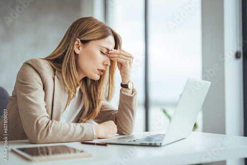 Exhausted businesswoman having a headache in modern office. Mature creative woman working at office desk with spectacles on head feeling tired. Stressed casual business woman feeling eye pain  photo