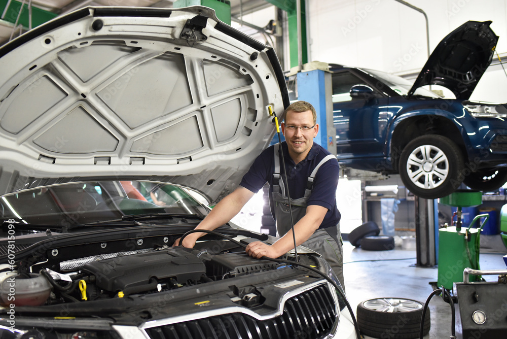 smiling car mechanic in a workshop - engine repair and diagnosis on a vehicle smiling car mechanic in a workshop - engine repair and diagnosis on a vehicle