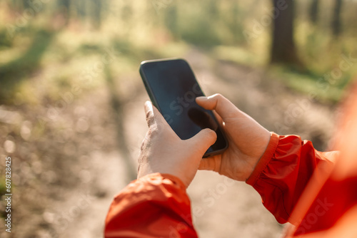 Closeup of a woman hand is holding mobile phone with copy space screen against blurred jungle landscape. Young male is searching information on cell telephone during summer adventure. High quality