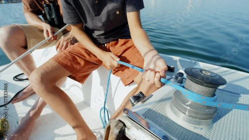 High angle shot of unrecognizable boy tightening line using sailboat winch during trip on summer day with his father photo