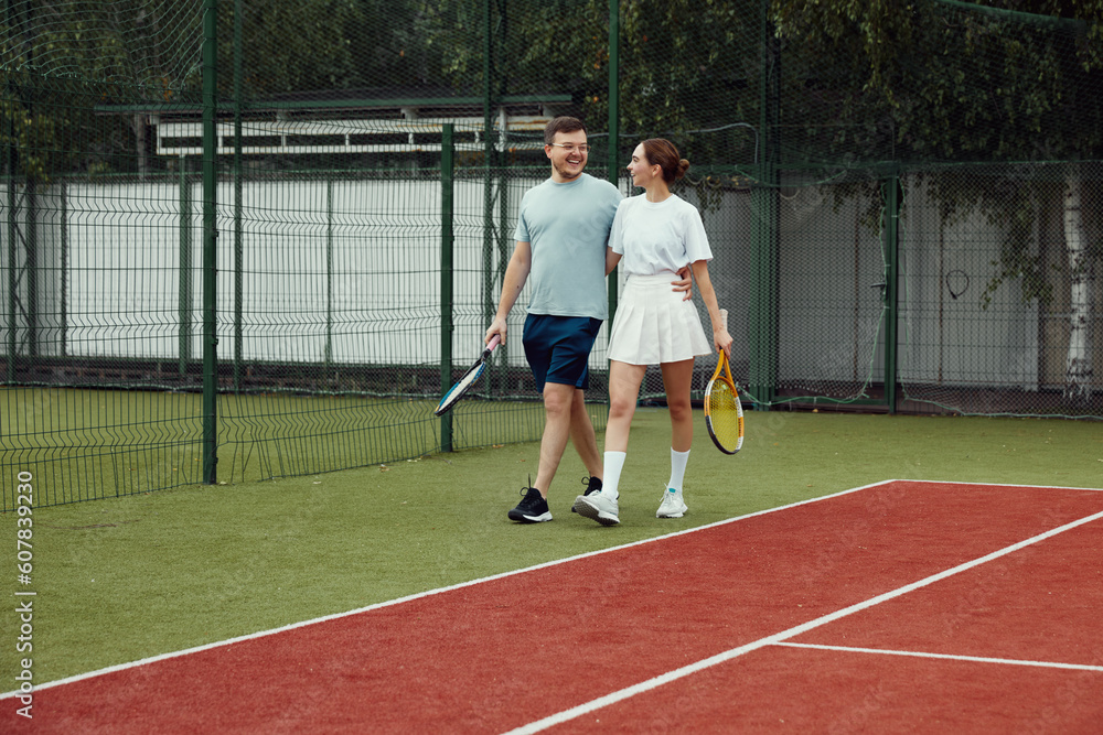 Young couple on tennis court. Two tennis players are smiling and walking around the court and talking
