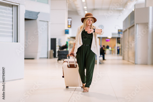 Focused elderly woman with suitcase checking time on wristwatch in airport photo