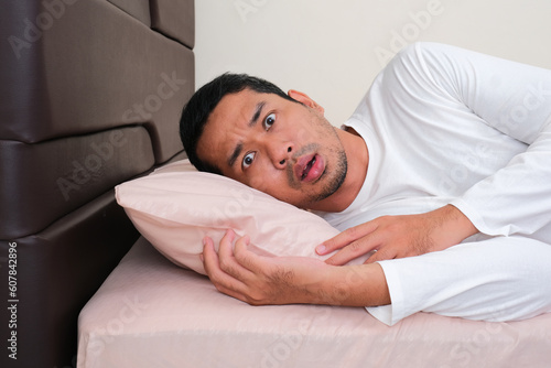 Adult Asian man showing shocked face expression when in bed photo