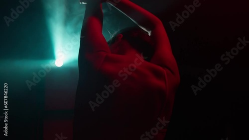 Female dancer sensually moves, dancing in dark in light rays, gesturing hands touching herself. Back view of graceful woman performing elements of modern choreography in neon illumination