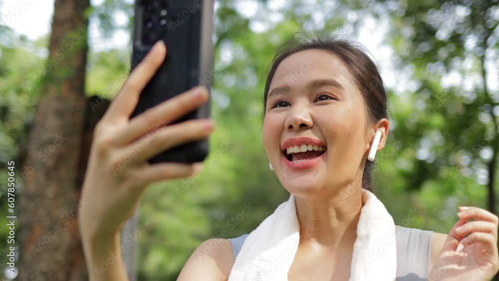 Beautiful Asian woman exercising outdoors in the park. She holds a smartphone online talking with friends. Sport concept, health care Beautiful Asian woman exercising outdoors in the park. She holds a smartphone online talking with friends. Sport concept, health care