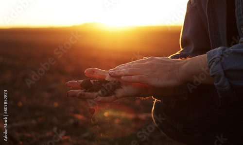 Male farmer's hand holds a handful of dry ground and checks soil fertility and quality before sowing crops on plowed field at sunset. Cultivated land. Concept of organic agriculture and agribusiness