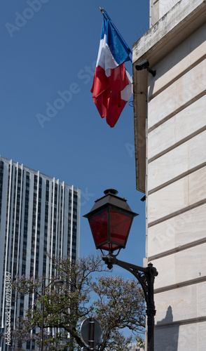 Paris, France - 05 19 2023: A red street lamp and a French flag along a stone wall.