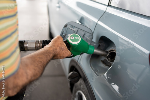 Detail of hand of eighty year old man putting 95 petrol in light blue car in short sleeves with brown hairy arms.