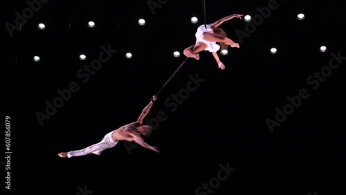 Aerial straps duo with white costume on black stage background doing performance 