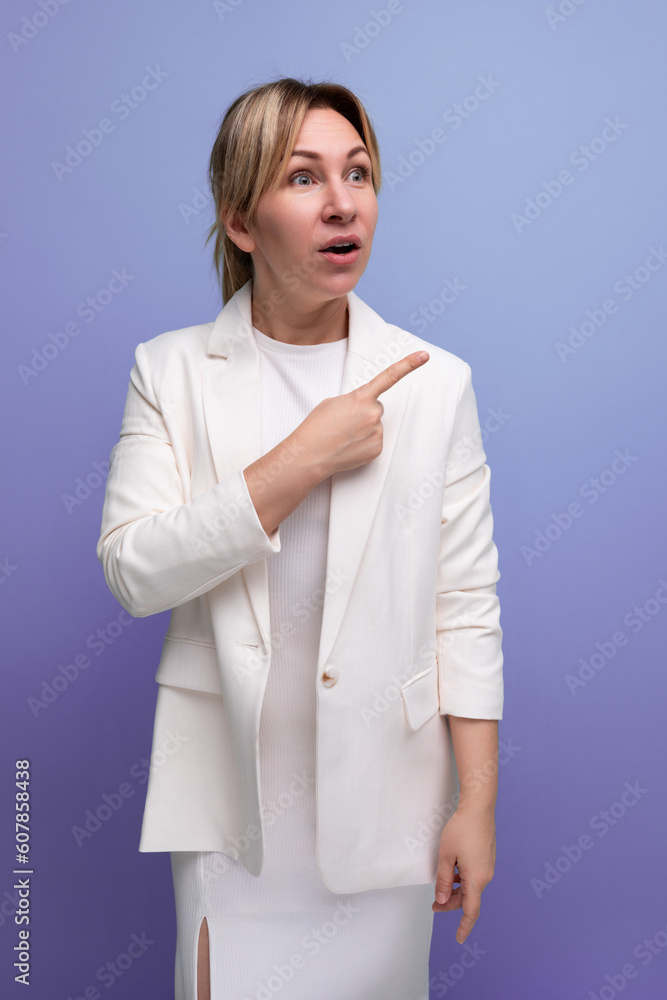 young surprised slim elegant female adult wearing jacket and dress pointing finger to the side young surprised slim elegant female adult wearing jacket and dress pointing finger to the side