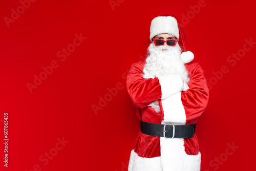 serious santa claus in red glasses stands with his arms crossed on colored background
