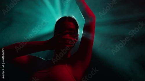 Young dancer performs contemporary dance solo routine. Choreographer gestures hands in modern dance show on dark stage with colorful dramatic lighting. Graceful ballerina dancing in neon light