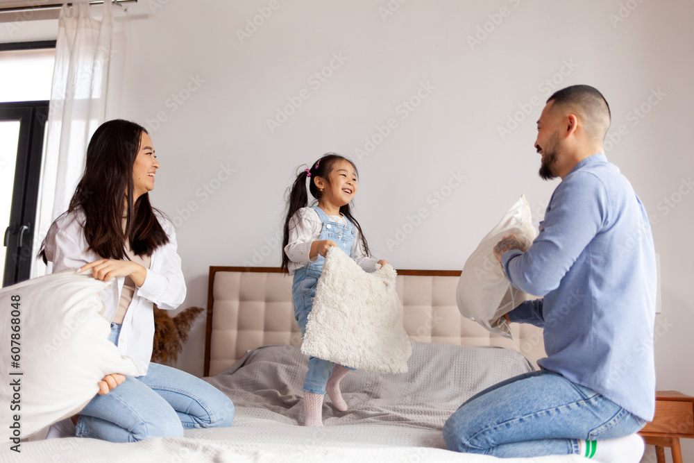 pillow fight, little Asian girl plays with her parents on the bed at home, Korean parents spend time with their daughter pillow fight, little Asian girl plays with her parents on the bed at home, Korean parents spend time with their daughter