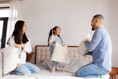 pillow fight, little Asian girl plays with her parents on the bed at home, Korean parents spend time with their daughter