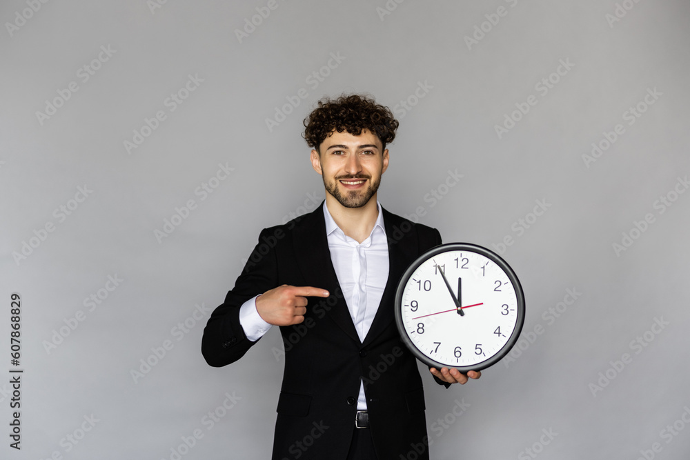 Laughing young bearded business man in classic black suit shirt tie posing isolated on grey background holding clock Laughing young bearded business man in classic black suit shirt tie posing isolated on grey background holding clock