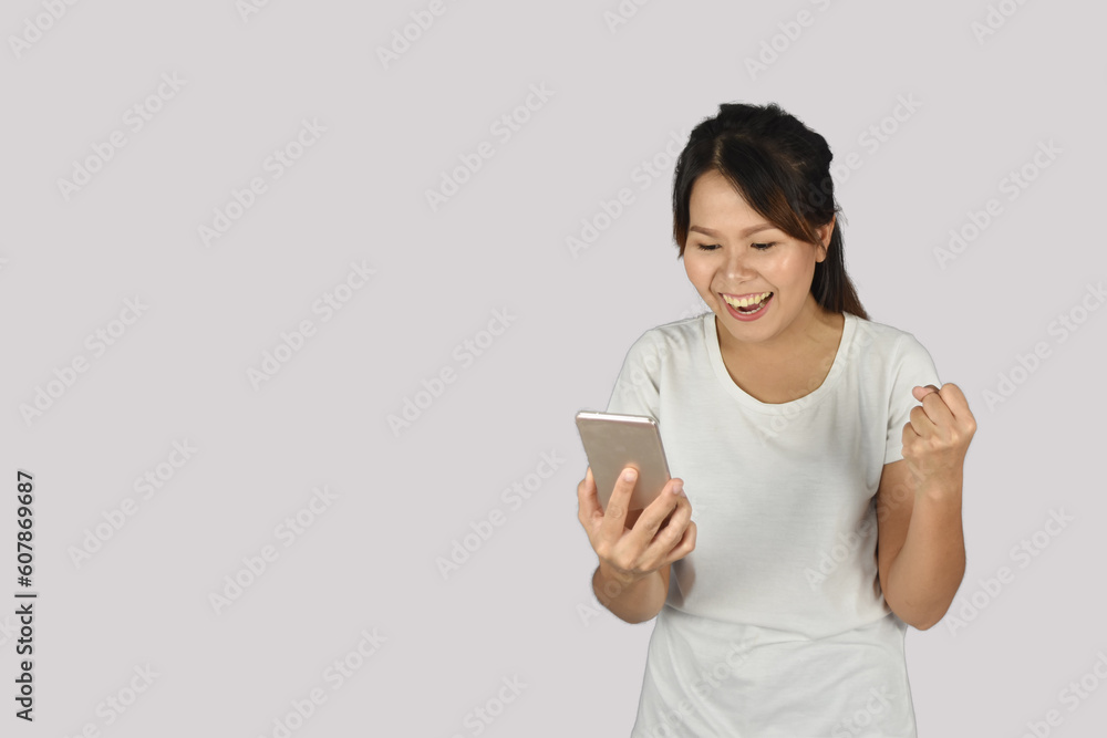 attractive and smiling women in t-shirts holding smartphones and showing yes gesture on grey background attractive and smiling women in t-shirts holding smartphones and showing yes gesture on grey background