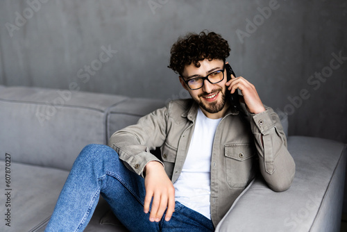 Young man in glasses angry talking on the phone sitting on the couch.