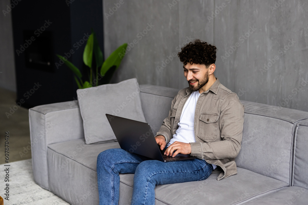 Typing new blog post. Handsome young man using his laptop with smile while sitting on the couch at home Typing new blog post. Handsome young man using his laptop with smile while sitting on the couch at home