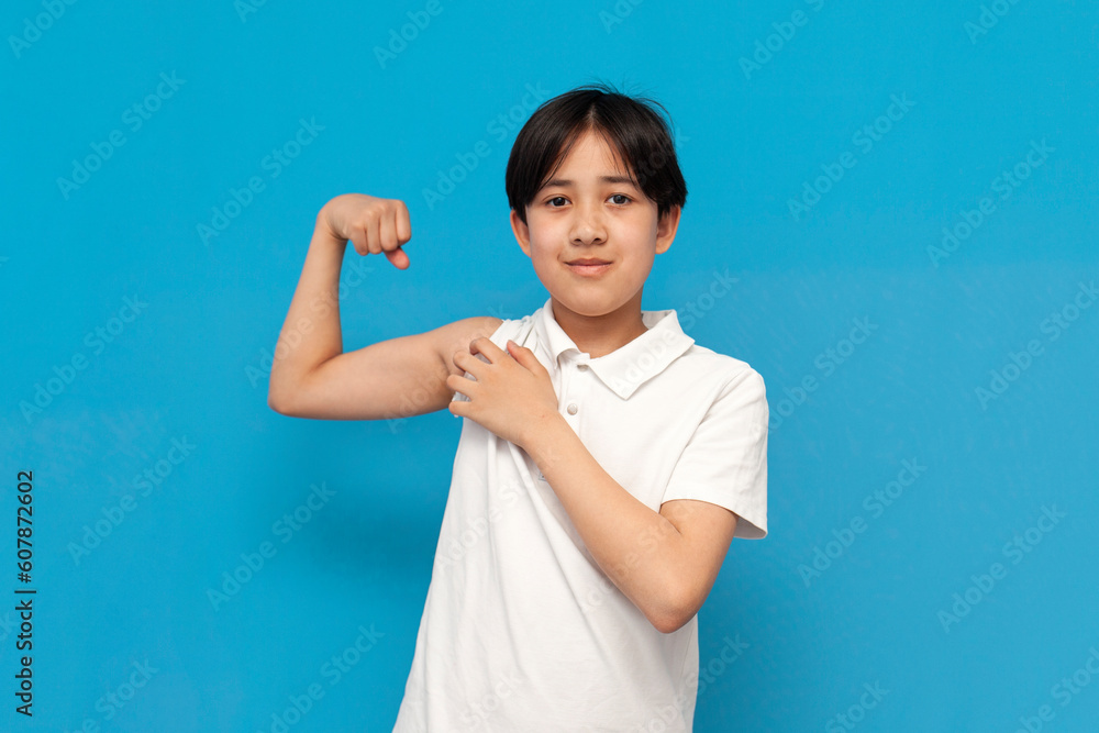 strong asian schoolboy of twelve years old showing biceps over blue isolated background, sporty korean kid strong asian schoolboy of twelve years old showing biceps over blue isolated background, sporty korean kid