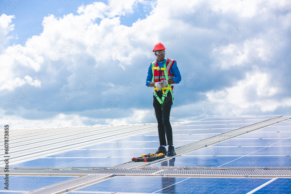 African American engineer maintaining solar cell panels on factory building rooftop. Technician working outdoor on ecological solar farm construction. Renewable clean energy technology concept African American engineer maintaining solar cell panels on factory building rooftop. Technician working outdoor on ecological solar farm construction. Renewable clean energy technology concept