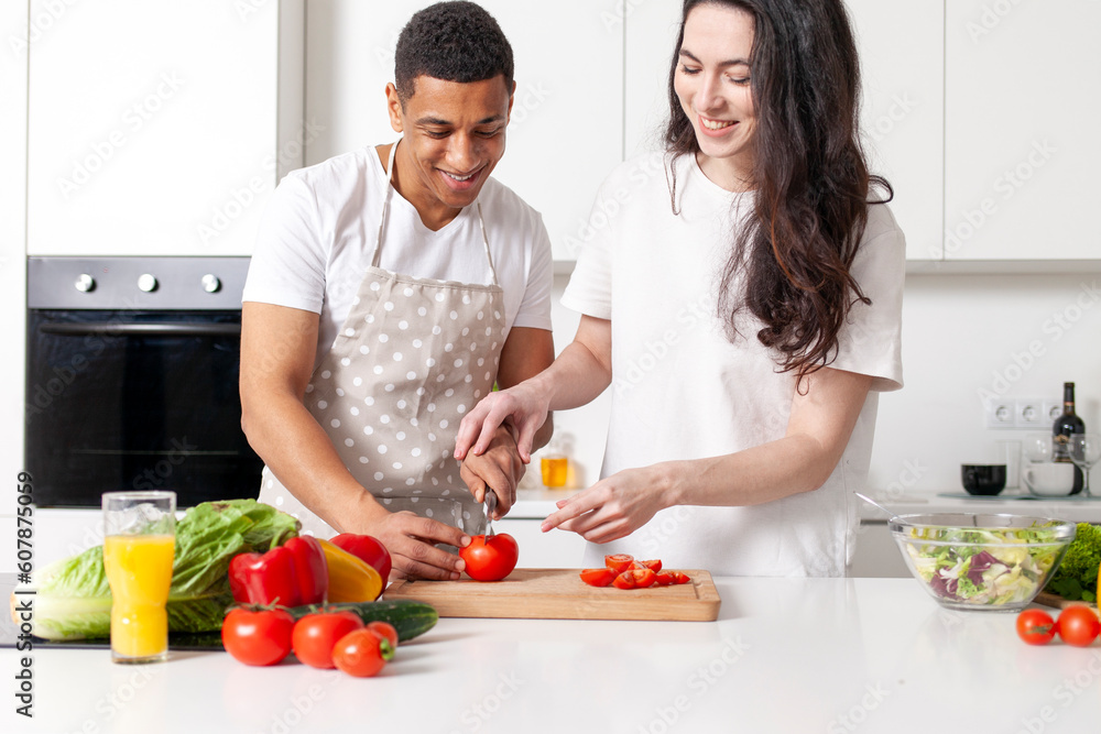 multiracial young couple preparing veggie vegetable and greens salad in white modern kitchen